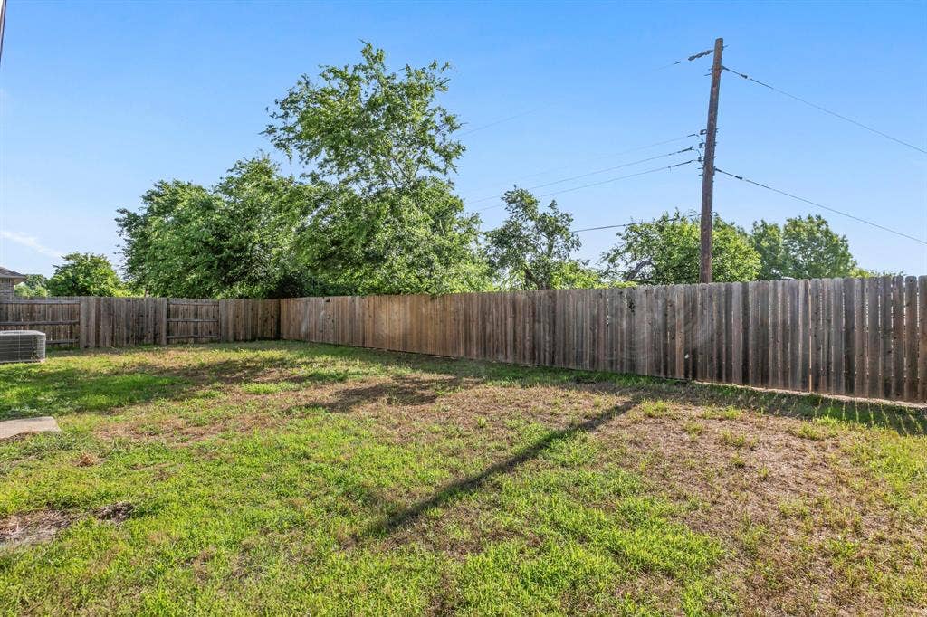 1516 Kinglet Street, DeSoto, TX 75115 Expansive backyard space featuring a wooden privacy fence, mature trees, and a ground-mounted HVAC unit