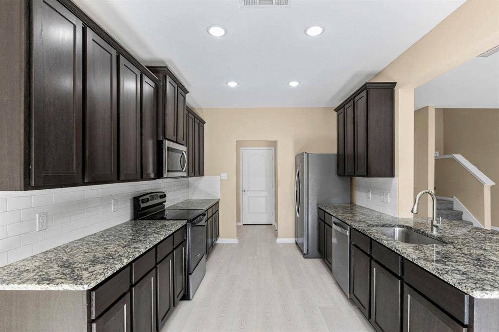 1516 Kinglet Street, DeSoto, TX 75115 Galley kitchen featuring dark wood-finish cabinetry, granite-style countertops, stainless steel appliances, and white subway tile backsplash