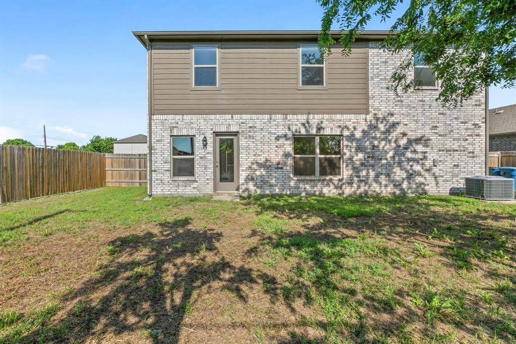 1516 Kinglet Street, DeSoto, TX 75115 Rear exterior featuring a mix of light-toned brick and horizontal siding, multiple windows, a rear entry door with an exterior light fixture, and a wood privacy fence