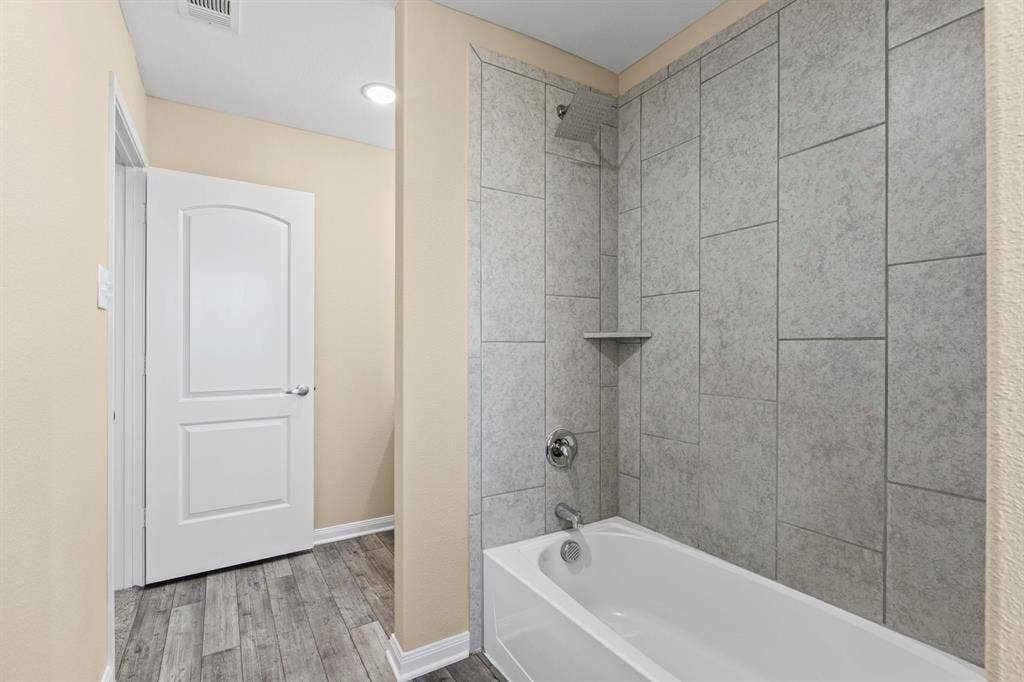 1516 Kinglet Street, DeSoto, TX 75115 Bathroom featuring a white bathtub, chrome fixtures, and grey large-format tile surround