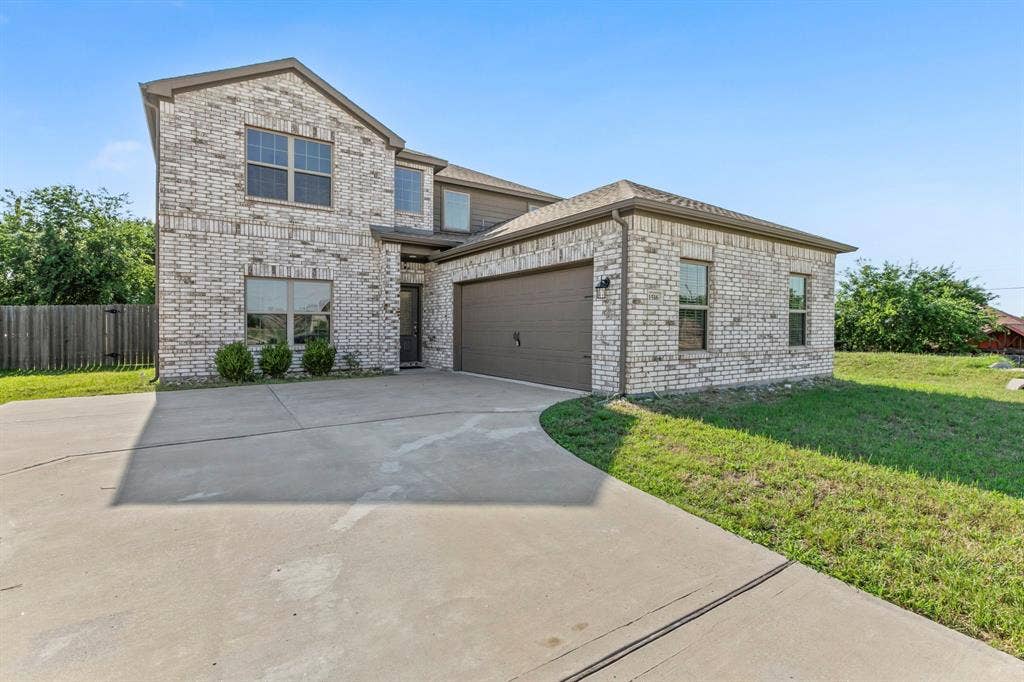 1516 Kinglet Street, DeSoto, TX 75115 Two-story residence featuring light brick masonry, a two-car garage with a dark brown door, and a concrete driveway