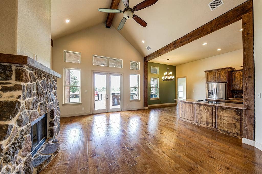 245 Fm 407 W, Argyle, TX 76226 Unfurnished living room featuring beam ceiling, ceiling fan, a stone fireplace, a chandelier in dining area, and wood-type flooring