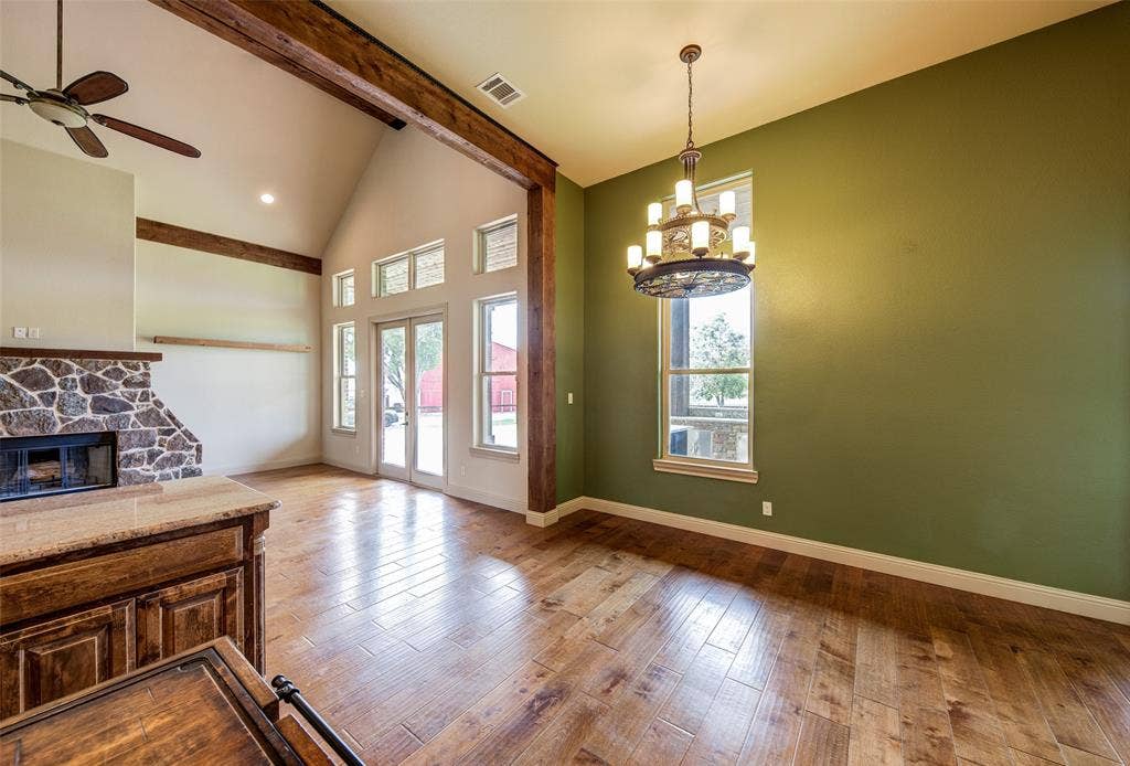 245 Fm 407 W, Argyle, TX 76226 Unfurnished dining area with beam ceiling, wood-type flooring, healthy amount of natural light, ceiling fan, and a stone fireplace