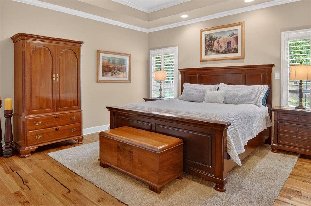 Spacious primary bedroom with wood flooring and wood shutters.
