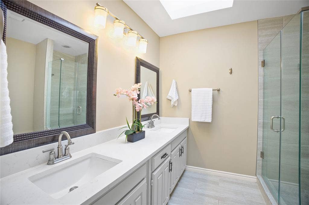 3228 Anchor Drive, Plano, TX 75023 Bathroom featuring a double vanity with undermount sinks and brushed nickel faucets, a frameless glass shower enclosure, a skylight, and wood-finish flooring