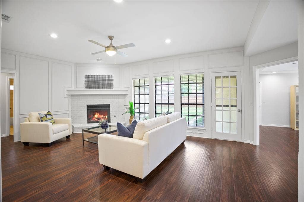 3228 Anchor Drive, Plano, TX 75023 Spacious living area featuring wood-finish flooring, a white brick fireplace with mantel, and decorative wall paneling