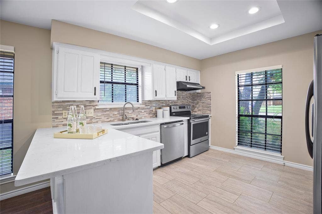 3228 Anchor Drive, Plano, TX 75023 Kitchen featuring white cabinetry, light-toned countertops, a mosaic tile backsplash, and stainless steel appliances