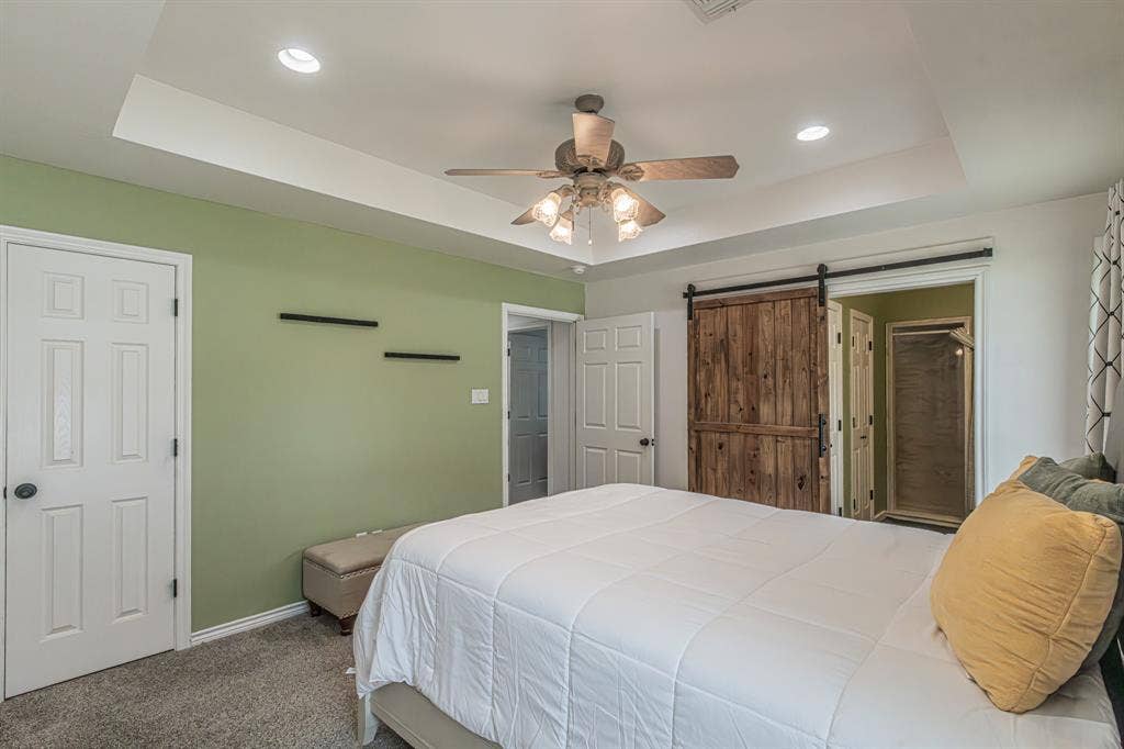 204 S Spring Branch Trail, Springtown, TX 76082 Recessed ceiling lighting, tray ceiling detail, wood-finish barn door, ceiling fan with light fixture, and plush carpet flooring
