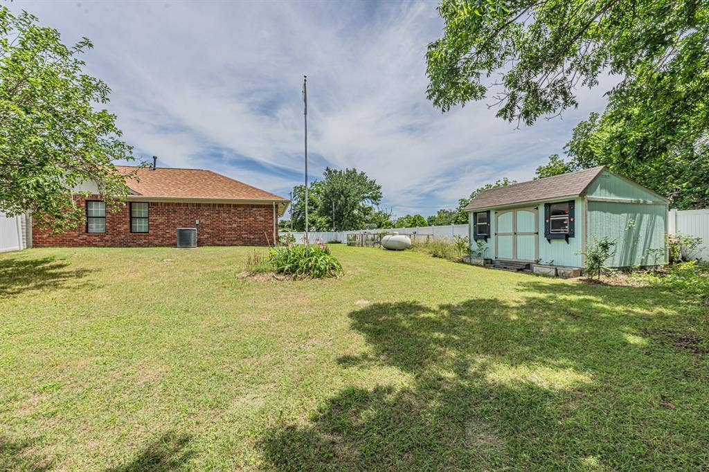 204 S Spring Branch Trail, Springtown, TX 76082 Expansive green lawn featuring a dedicated storage shed, partial brick exterior, and a white privacy fence