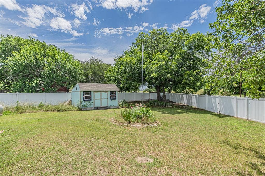 204 S Spring Branch Trail, Springtown, TX 76082 Expansive grass lawn featuring a light blue storage shed, a mature tree, and full perimeter white privacy fencing
