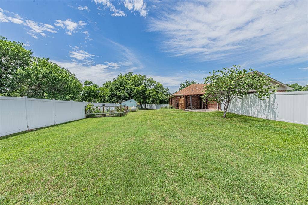 204 S Spring Branch Trail, Springtown, TX 76082 Spacious grass yard enclosed by white privacy fencing, featuring a single tree and a brick exterior building with a brown roof