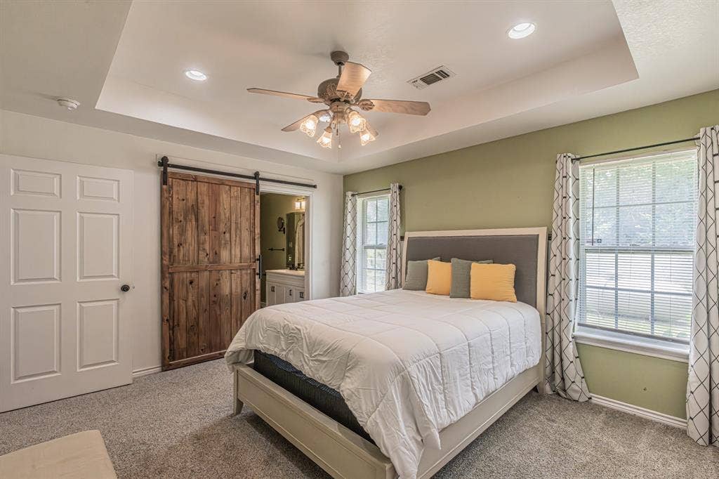 204 S Spring Branch Trail, Springtown, TX 76082 Recessed lighting and ceiling fan above, dual windows with blinds, a white six-panel door, and a rustic wood-finish barn door