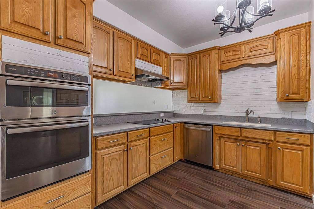 204 S Spring Branch Trail, Springtown, TX 76082 Kitchen featuring wood cabinetry, stainless steel appliances including a built-in oven and microwave, dark wood-finish flooring, and a white brick-patterned backsplash