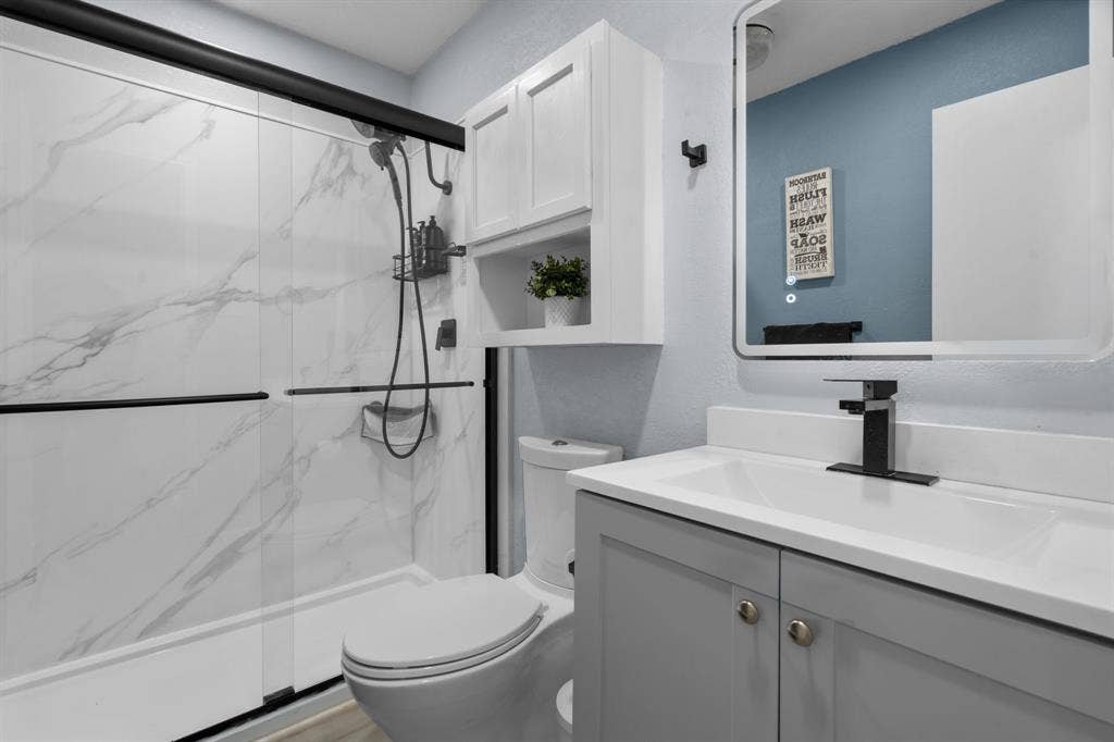 7629 Cedarhill Road, Watauga, TX 76148 Modern bathroom featuring a walk-in shower with marble-look paneling and black-framed sliding glass doors