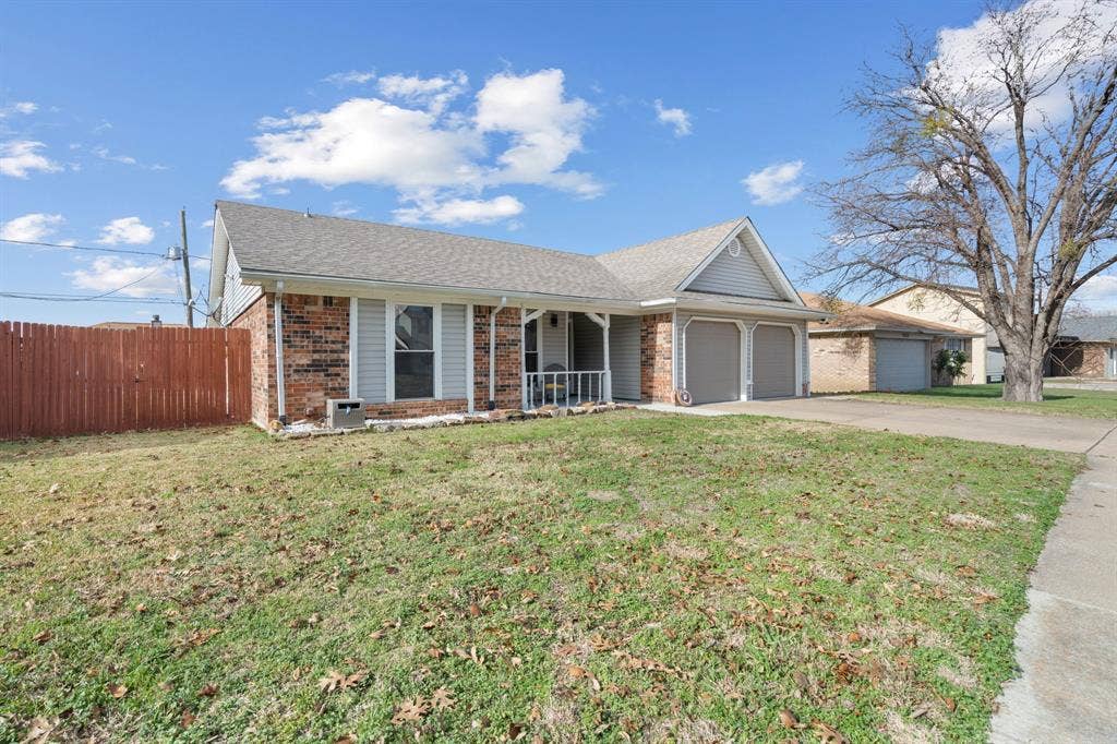 7629 Cedarhill Road, Watauga, TX 76148 Brick and siding exterior featuring a covered porch with white railing, a two-car garage with individual doors, and a partial wooden privacy fence