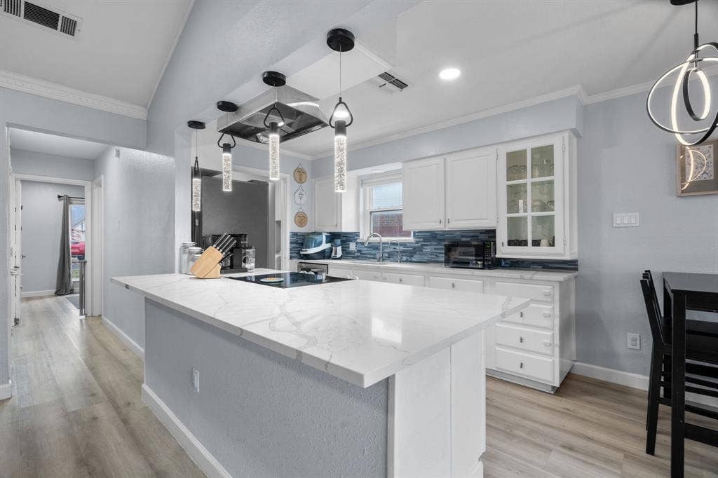 7629 Cedarhill Road, Watauga, TX 76148 Modern kitchen featuring a large central island with a cooktop, white cabinetry, a blue tile backsplash, recessed lighting, and wood-finish flooring