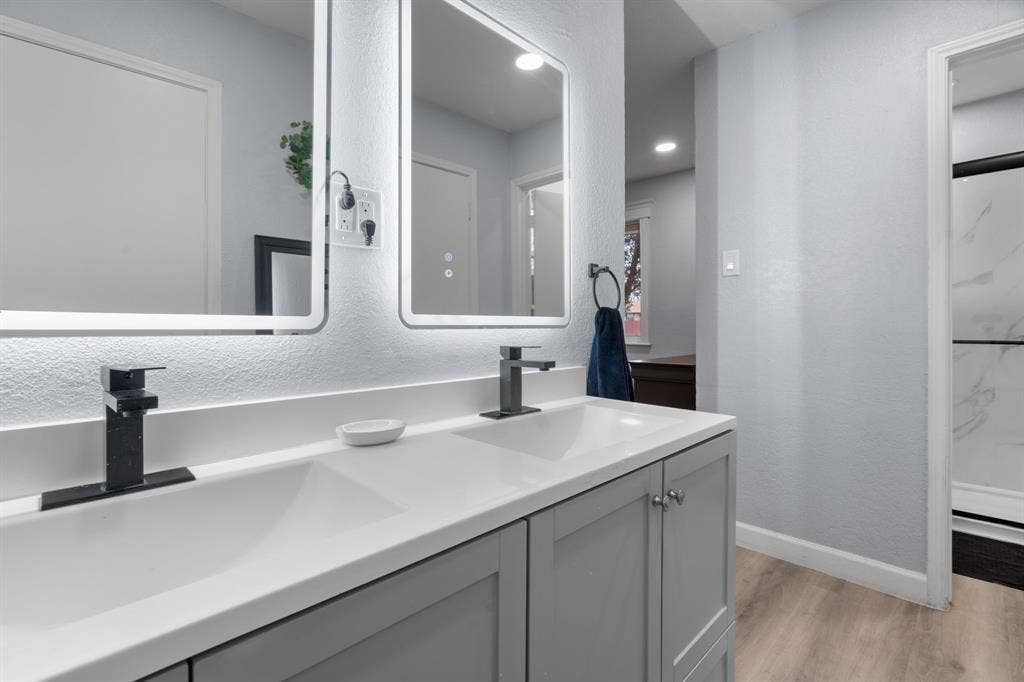 7629 Cedarhill Road, Watauga, TX 76148 Dual vanity with integrated sinks, white countertops, gray shaker cabinetry, matte black faucets, and illuminated rectangular mirrors