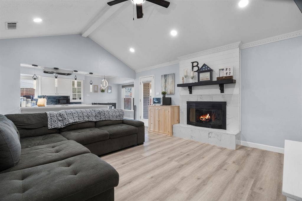 7629 Cedarhill Road, Watauga, TX 76148 Vaulted ceiling living area featuring a fireplace with a white shiplap and marbled-look surround, recessed lighting, wood-finish flooring, and a ceiling fan