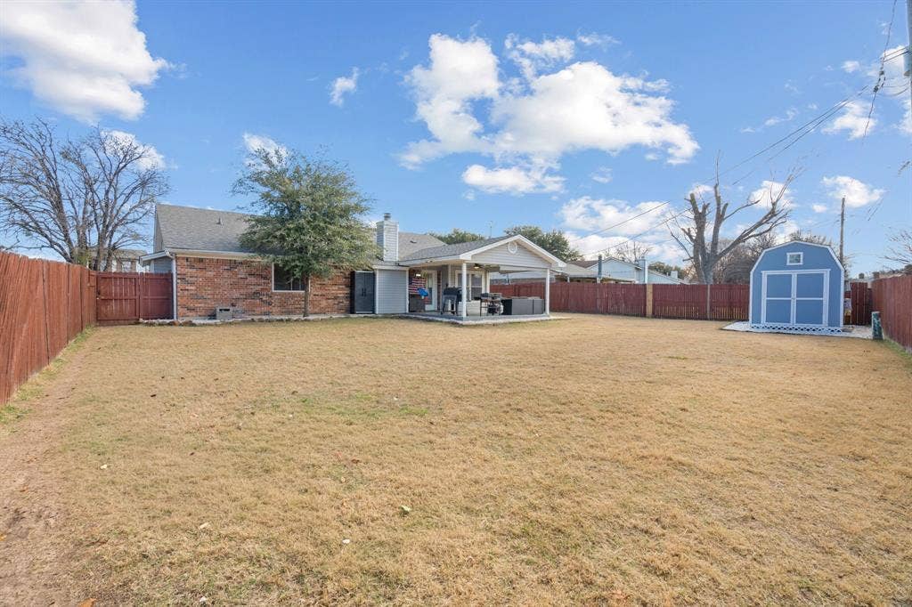 7629 Cedarhill Road, Watauga, TX 76148 Expansive backyard featuring a large lawn, wood privacy fencing, a covered patio area, and a standalone storage shed