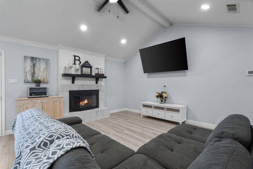 7629 Cedarhill Road, Watauga, TX 76148 Vaulted ceiling living area featuring a central fireplace with a dark mantel, light-toned wood-finish flooring, and recessed lighting
