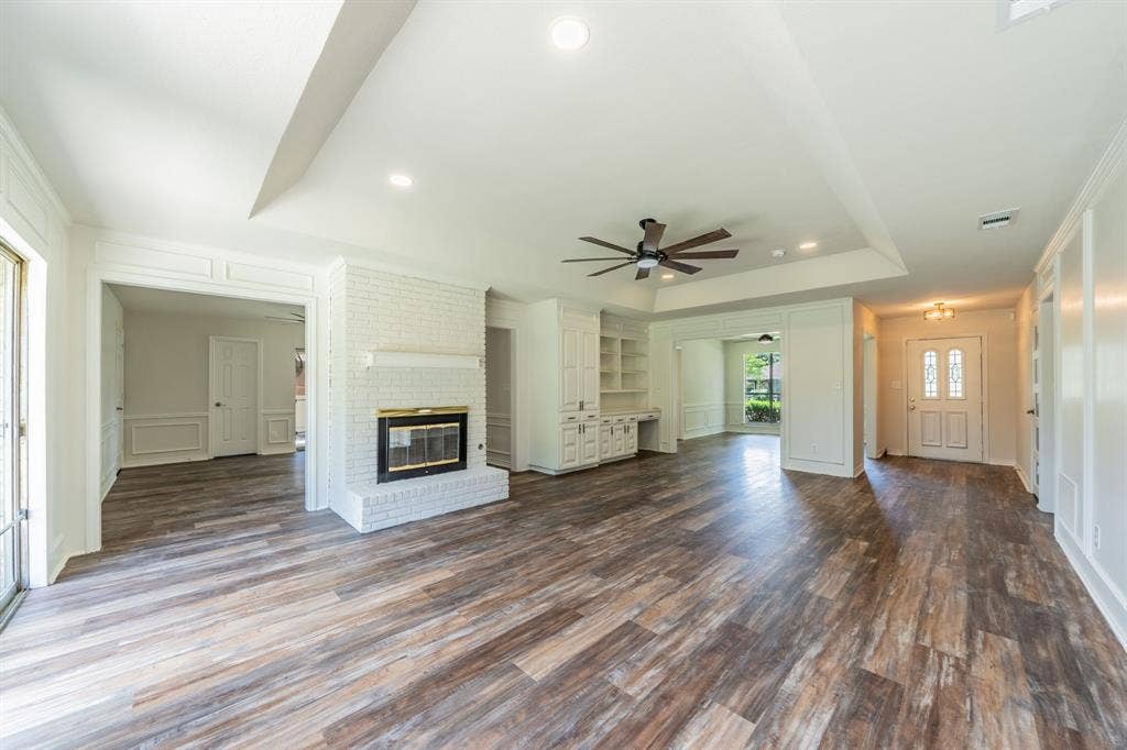 2212 Vickers Drive, Plano, TX 75075 Spacious open concept living area featuring wood-finish flooring, a white painted brick fireplace with a brass-trimmed insert, and a tray ceiling with a ceiling fan