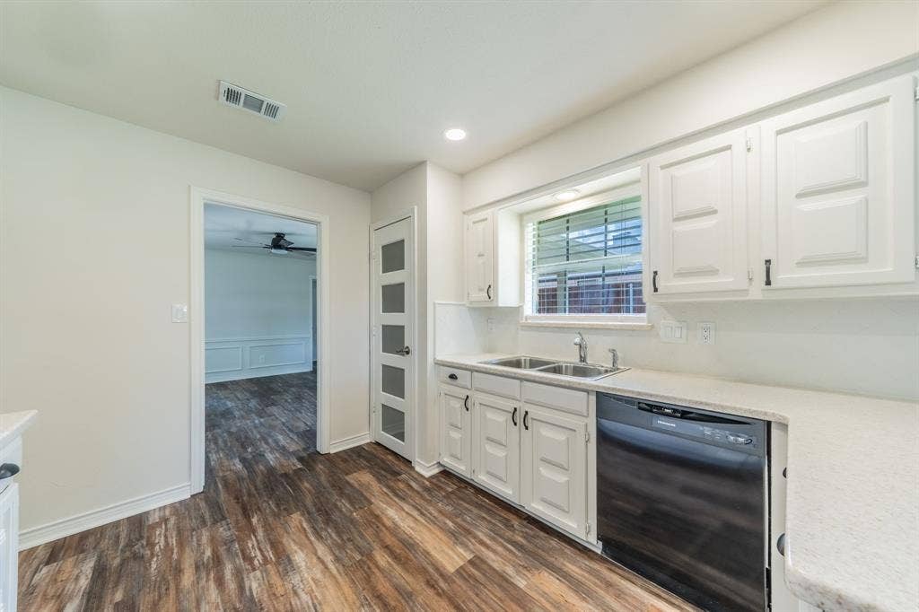2212 Vickers Drive, Plano, TX 75075 Kitchen featuring wood-finish flooring, white cabinetry, a double basin sink, a black built-in dishwasher, and a window with horizontal blinds