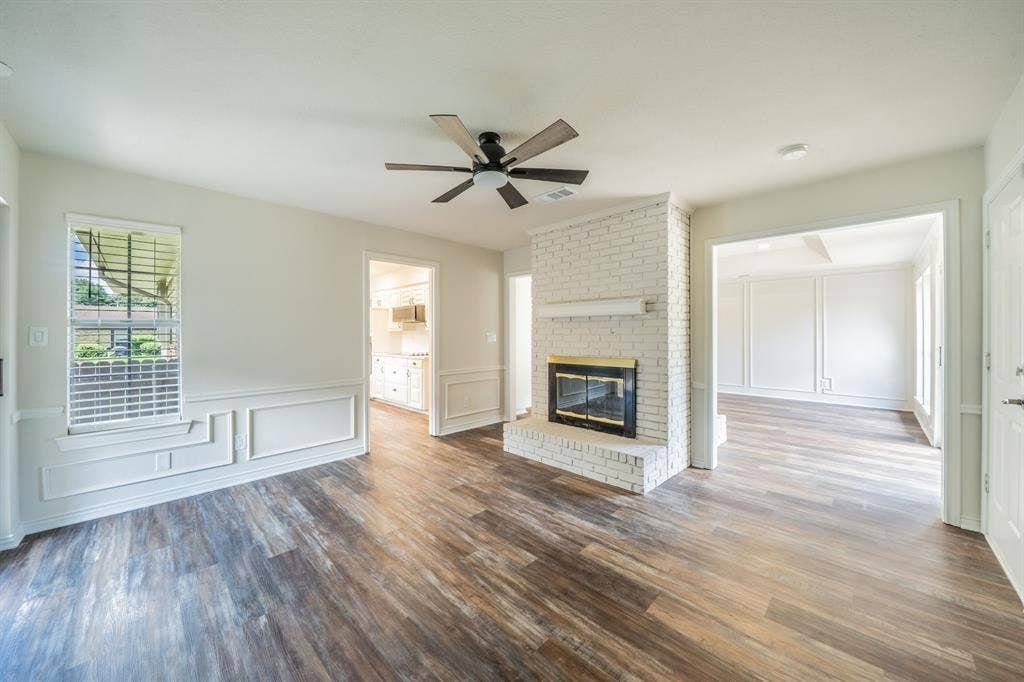 2212 Vickers Drive, Plano, TX 75075 Living area featuring wood-finish flooring, a white-painted brick fireplace with a black firebox, a ceiling fan, and wainscoting with decorative trim