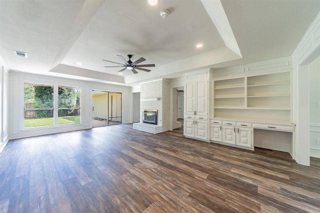 2212 Vickers Drive, Plano, TX 75075 Spacious living area featuring wood-finish flooring, a white brick fireplace, and built-in cabinetry with shelving