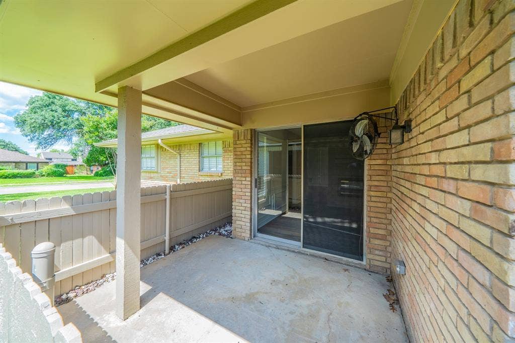 2212 Vickers Drive, Plano, TX 75075 Covered side patio area featuring a concrete slab, brick exterior wall, and a sliding glass door with a screen