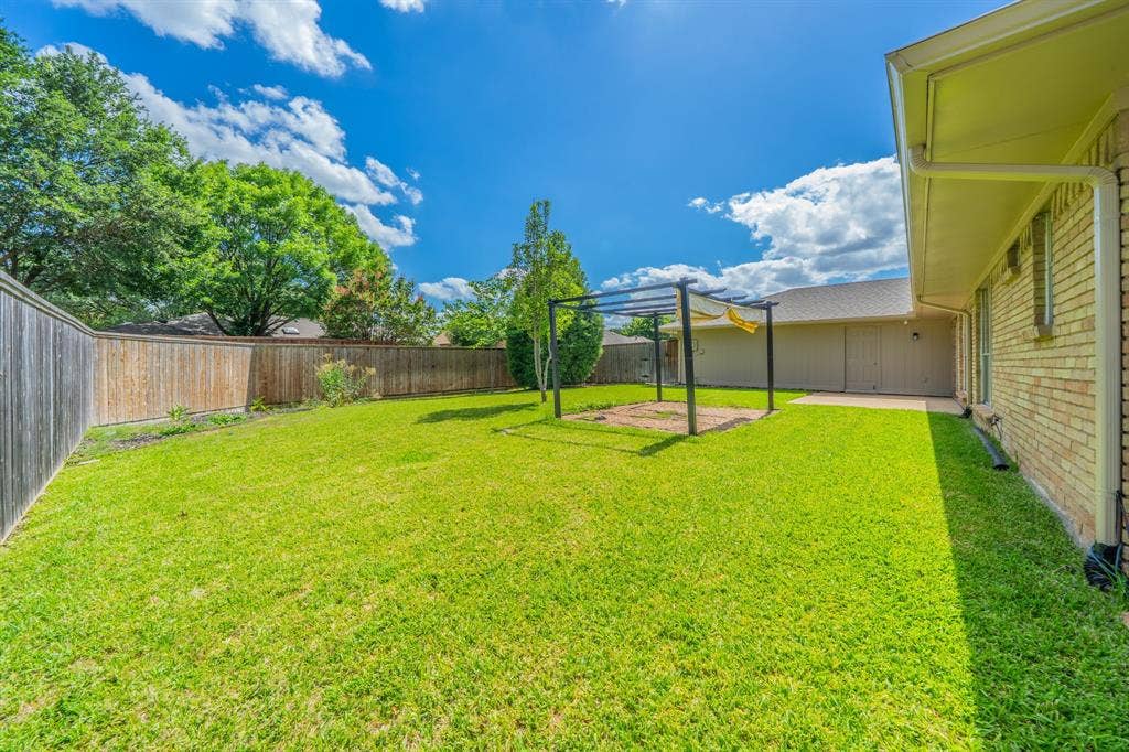 2212 Vickers Drive, Plano, TX 75075 Expansive green lawn featuring a privacy fence, a metal pergola, mature perimeter trees, and a brick exterior with a concrete patio