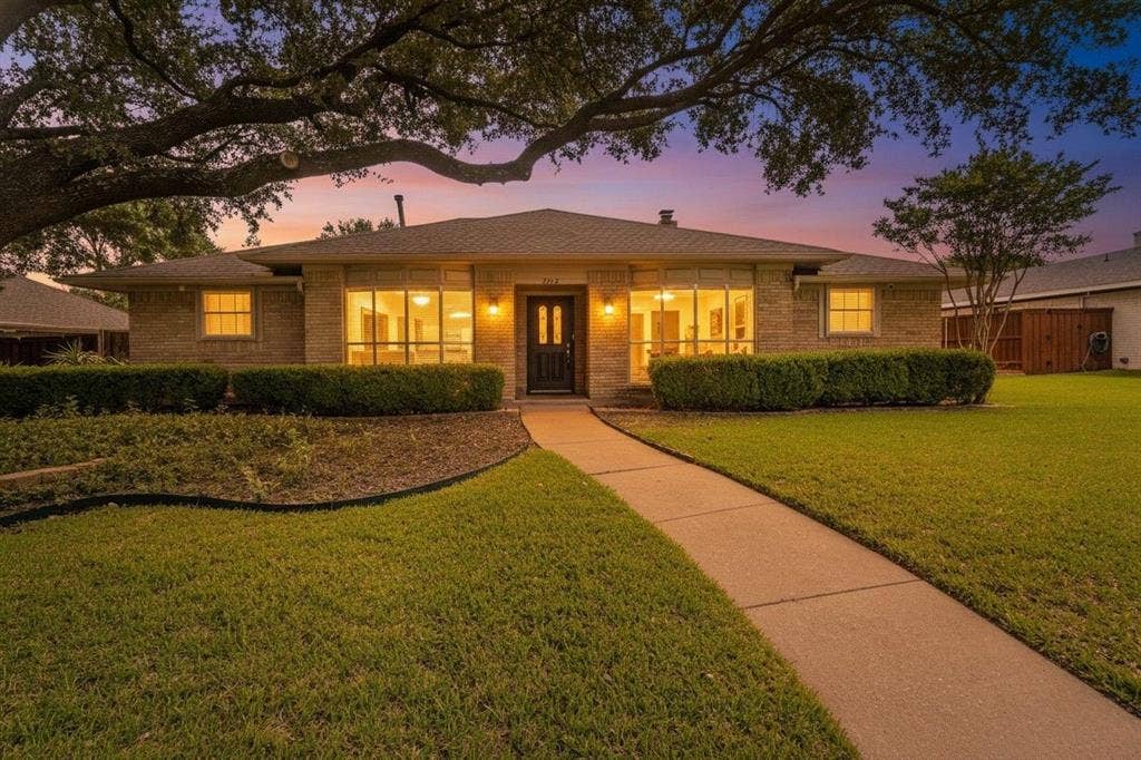 2212 Vickers Drive, Plano, TX 75075 Brick exterior with a dark entry door, multiple front-facing windows, a concrete walkway, and a manicured lawn with mature trees and shrubbery