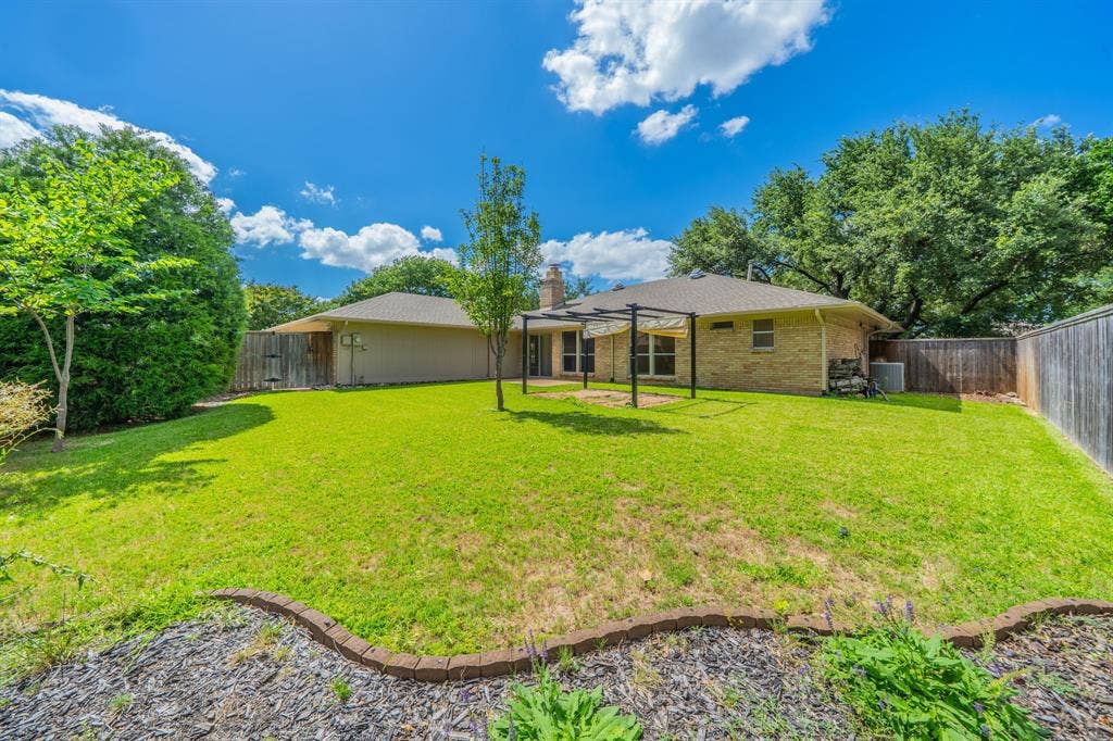 2212 Vickers Drive, Plano, TX 75075 Spacious backyard featuring a pergola structure, manicured lawn, and mature trees