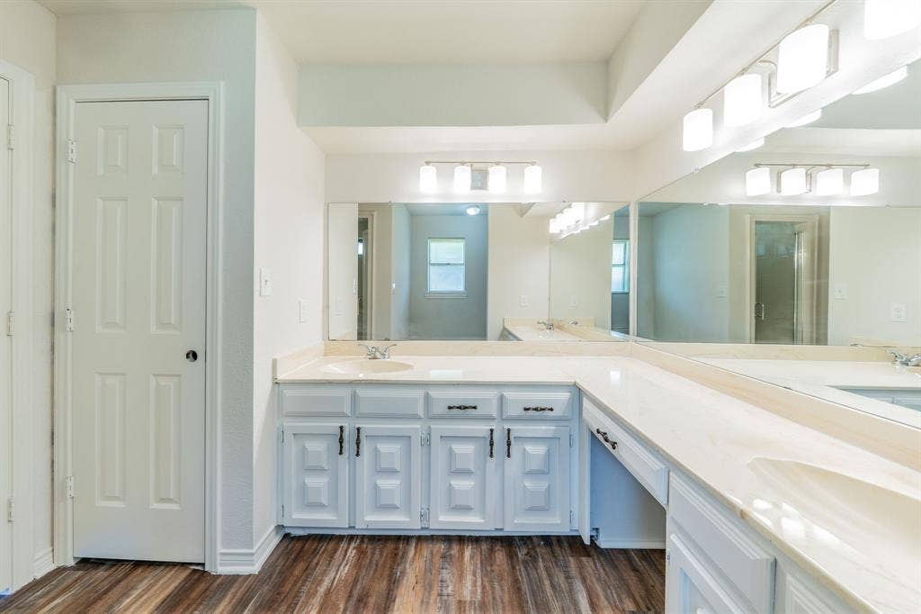 2212 Vickers Drive, Plano, TX 75075 Bathroom vanity area featuring dual sinks set within a light-toned countertop, extensive wall-mounted mirrors, and wood-finish flooring