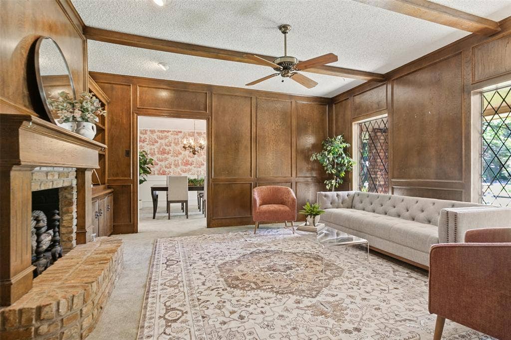 915 Grinnell Drive, Richardson, TX 75081 915 Grinell Dr. - Formal living area featuring wood picture-frame paneling, wood beams, ceiling fan, brick fireplace with gas-log insert, and beautiful windows providing abundant natural light.