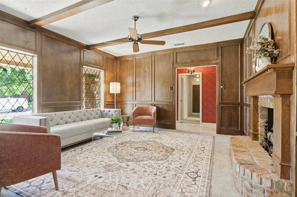 915 Grinnell Drive, Richardson, TX 75081 915 Grinell Dr. - Formal living area featuring wood picture-frame paneling, wood beams, ceiling fan, brick fireplace with gas-log insert, and beautiful windows providing abundant natural light.
