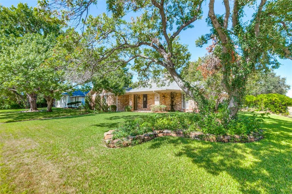 915 Grinnell Drive, Richardson, TX 75081 915 Grinnell Dr. - Front exterior of the home situated on a large corner lot, featuring mature trees, established landscaping, and a spacious covered front porch.
