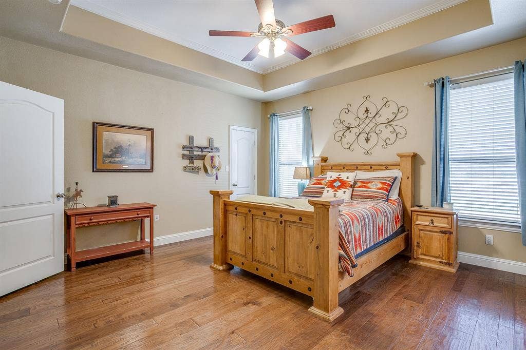 Recessed ceiling with crown molding, wood-finish flooring, two windows with blinds, and a ceiling fan with integrated lighting