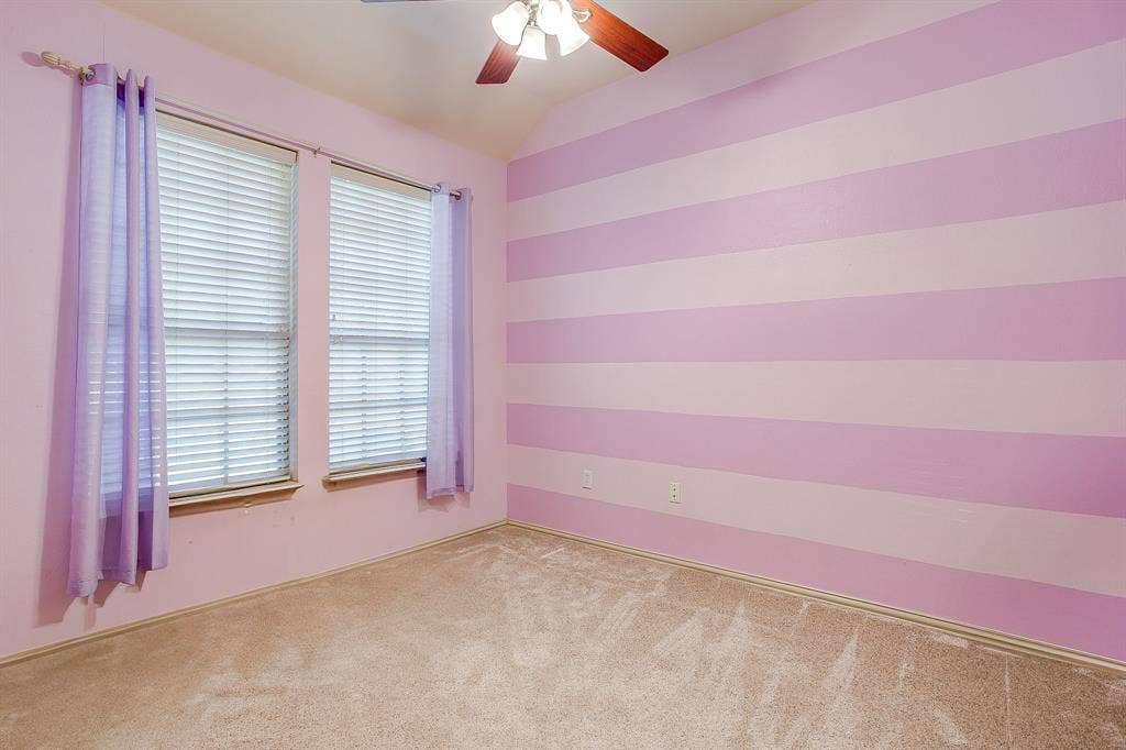 Vaulted ceiling featuring a ceiling fan with integrated lighting, two windows with blinds, and carpeted flooring