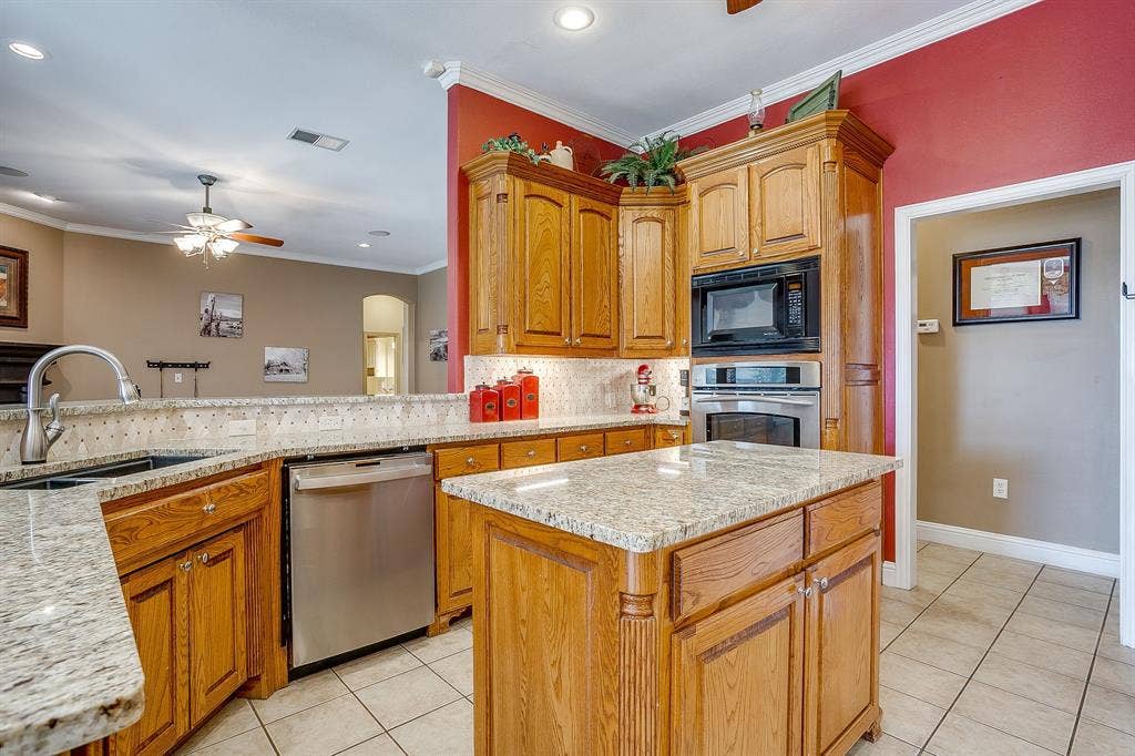 Kitchen featuring wood cabinetry, light-toned granite countertops, stainless steel appliances, a center island, and tile flooring