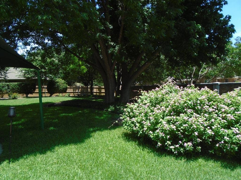 5949 River Bend Drive, Benbrook, TX 76132 Expansive backyard featuring a lush lawn, mature trees, flowering shrubs, and a wooden privacy fence