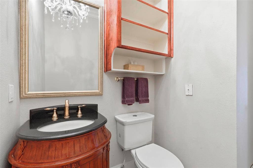 5949 River Bend Drive, Benbrook, TX 76132 Half Bath w Curved wood-finish vanity with an undermount sink, brass-finish faucet, and black countertop
