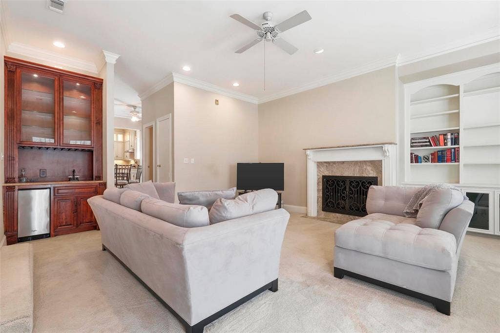 5949 River Bend Drive, Benbrook, TX 76132 Living space featuring a built-in wet bar with cabinetry and integrated mini-refrigerator, a fireplace with a stone surround and ornate screen, and built-in shelving with lower closed storage
