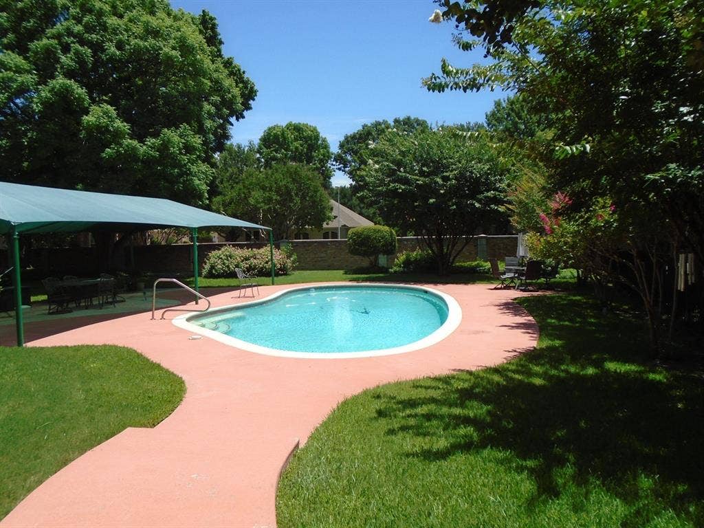 5949 River Bend Drive, Benbrook, TX 76132 Kidney-shaped swimming pool with a red-toned concrete surround, complemented by a green lawn and mature trees