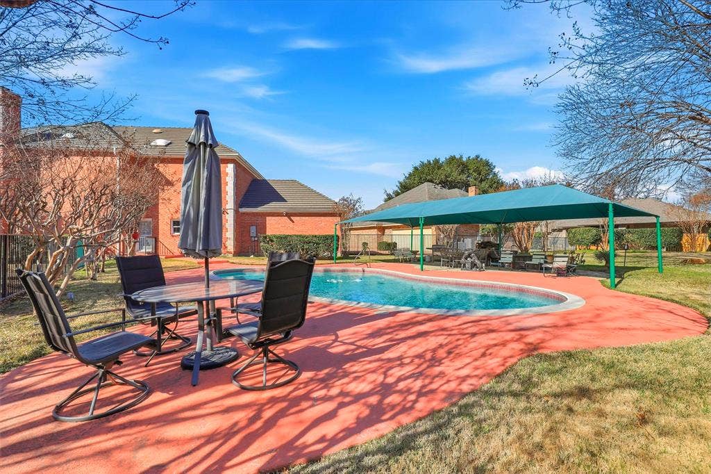 5949 River Bend Drive, Benbrook, TX 76132 Outdoor swimming pool area featuring a blue shade structure, surrounding red-hued concrete decking, and an adjacent grassy expanse