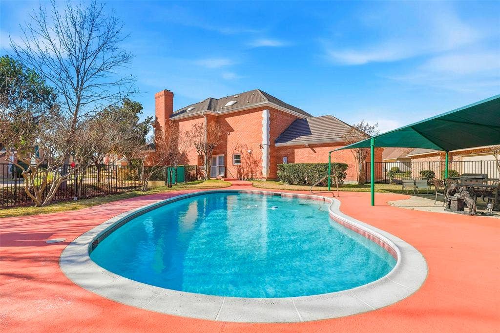 5949 River Bend Drive, Benbrook, TX 76132 Freeform swimming pool with red-toned concrete patio surround, a green shade structure, and a brick-faced exterior with a chimney