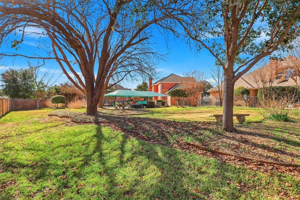 5949 River Bend Drive, Benbrook, TX 76132 Expansive backyard featuring mature trees, a manicured lawn, and a stone bench