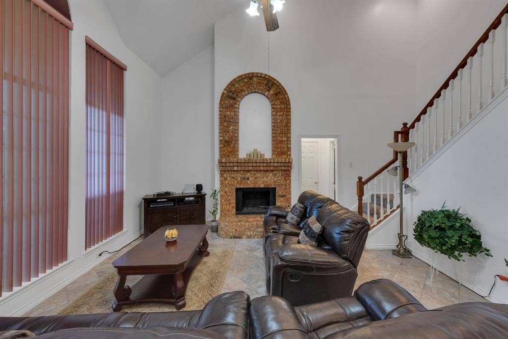 4622 Devonshire Drive, Grand Prairie, TX 75052 Vaulted ceiling living area featuring a brick fireplace with an arched opening, a ceiling fan, and large vertical blinds
