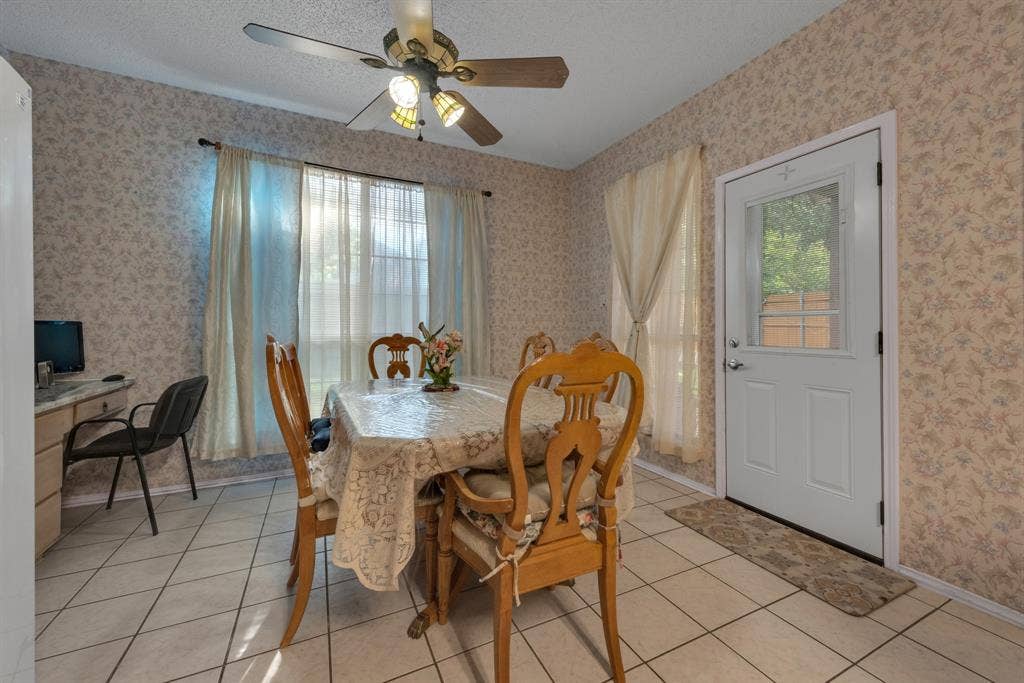 4622 Devonshire Drive, Grand Prairie, TX 75052 Dining area with patterned wallpaper, ceramic tile flooring, a window with sheer curtains, a white panel door with a glass insert, and a ceiling fan with integrated lighting