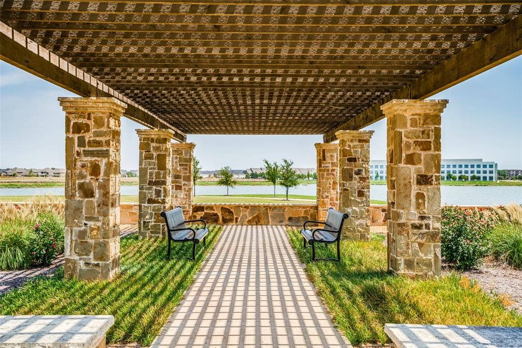 12986 Jk Ojha Street, Farmers Branch, TX 75234 Stone-clad pergola structure with a slatted roof, featuring a paved pathway and flanking green spaces