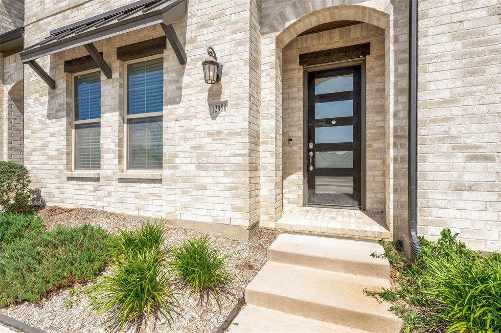 12986 Jk Ojha Street, Farmers Branch, TX 75234 Arched entryway featuring a modern black front door with frosted glass panels, surrounded by light-colored brick masonry